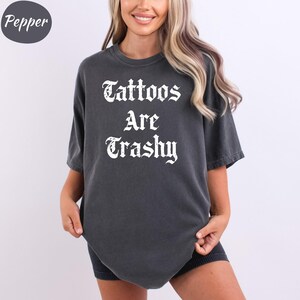 a woman wearing a black shirt that says tattoos are grasy