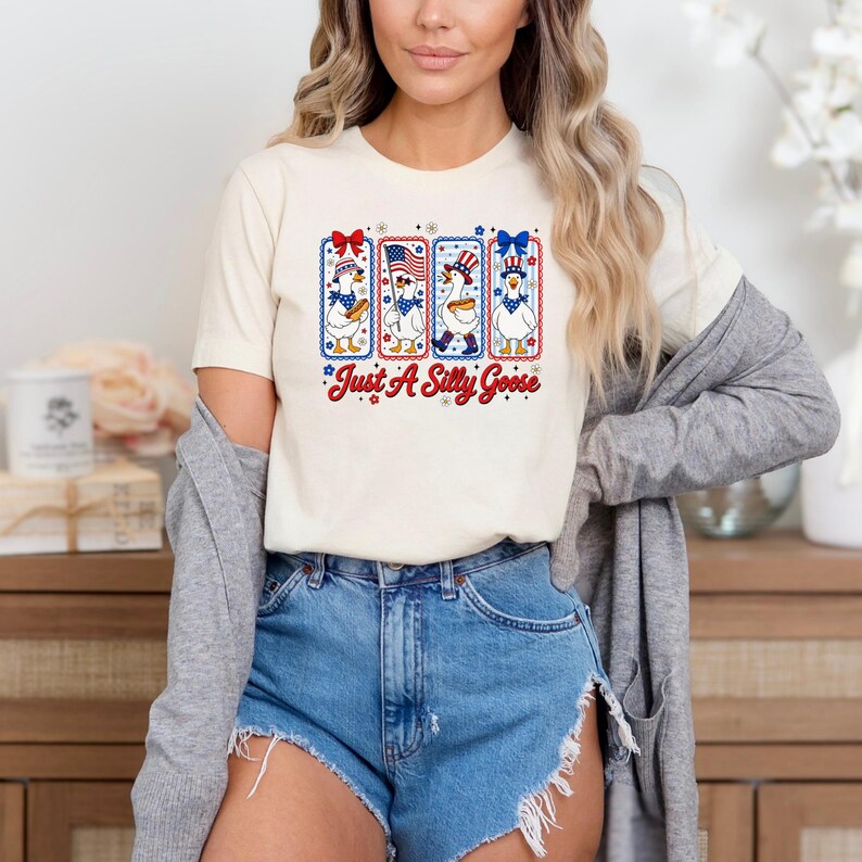 A woman wearing a white t-shirt with a graphic design and denim shorts, standing in front of a wooden cabinet.