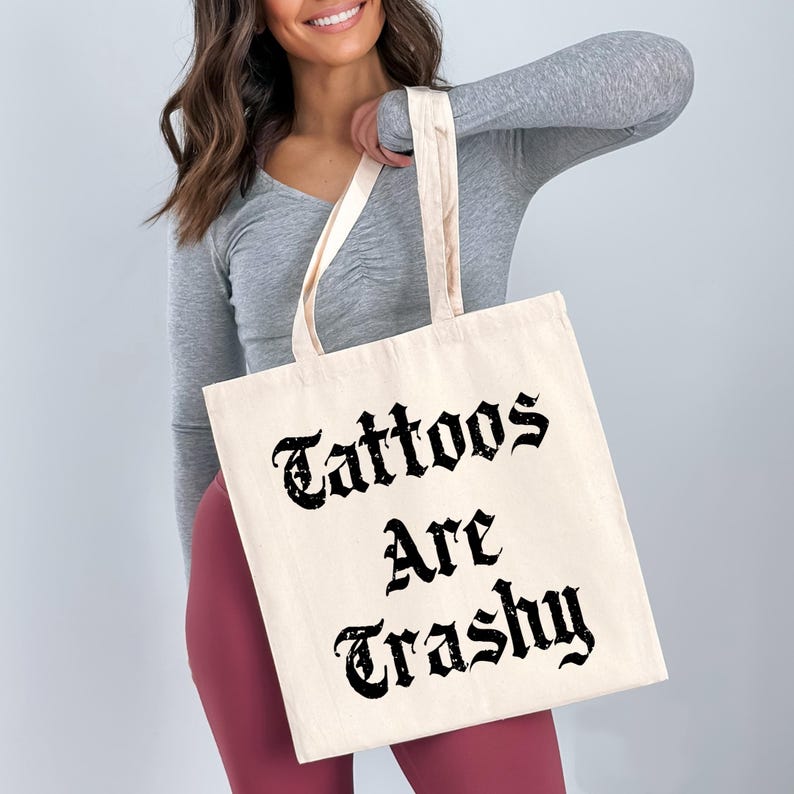 a woman holding a tote bag that says tattoos are trashy