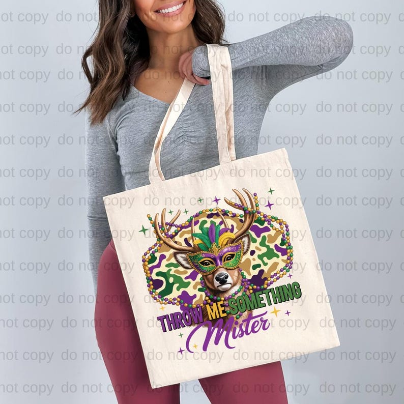 A woman is holding a white tote bag with a colorful design featuring a deer head and the text "THrowing me something MISTER" printed on it.