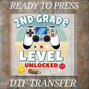 May include: A graphic transfer design featuring the text READY TO PRESS at the top and 2ND GRADE LEVEL UNLOCKED at the bottom. The center shows a white game controller over a dotted circle, a yellow padlock, a colorful pencil, and a red apple.