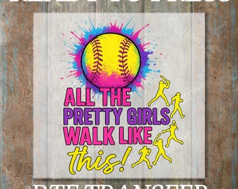 May include: A softball design with the text "ALL THE PRETTY GIRLS WALK LIKE this!" in pink and yellow. The design includes a yellow softball with colorful paint splatters and yellow silhouettes of softball players.