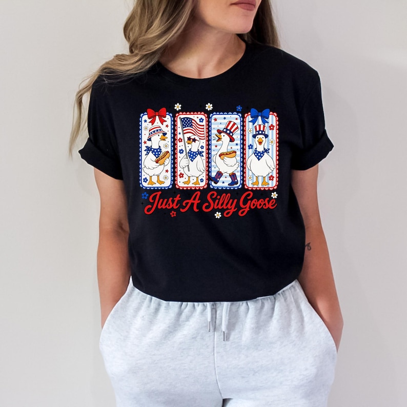 A woman wearing a black t-shirt with a graphic design featuring four cartoon ducks in patriotic colors and accessories.