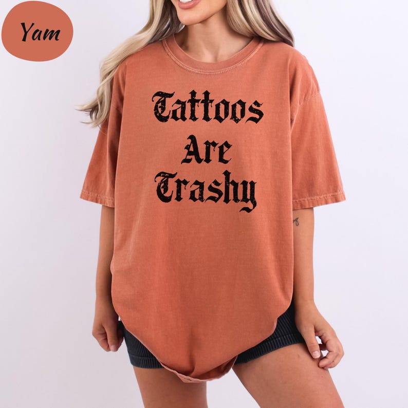 a woman wearing an orange shirt that says tattoos are trashy