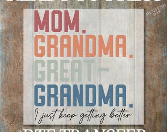 May include: Ready to press iron-on transfer design featuring the text "Mom. Grandma. Great-Grandma. I just keep getting better." in a colorful layered design with a rustic wood background.
