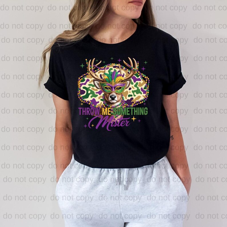 A woman wearing a black t-shirt with a colorful graphic design featuring a deer wearing a Mardi Gras mask and the text "THrowing ME SOMETHING MISTER" printed on it.