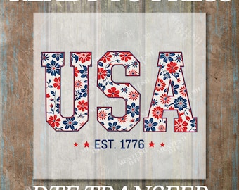 May include: A patriotic design featuring the word "USA" in bold, floral-patterned letters with red, white, and blue colors. The text "EST. 1776" is below the letters, with stars on each side. The words "READY TO PRESS" and "DTF TRANSFER" are also present.