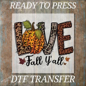 May include: A fall-themed design featuring the word "LOVE" with leopard print letters and a pumpkin. Below, the phrase "Fall y'all" is written in a script font, with autumn leaves. The words "READY TO PRESS" and "DTF TRANSFER" are also present.