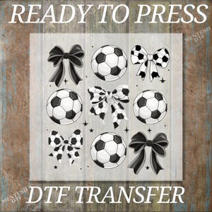 May include: A DTF transfer design featuring soccer balls and bows. The soccer balls are black and white, and the bows are black and white or solid black. The text "READY TO PRESS" and "DTF TRANSFER" are at the top and bottom.
