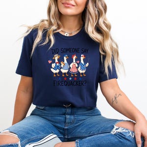 A woman wearing a navy blue t-shirt with a graphic of four cartoon ducks and the text "Did someone say firequacker?"