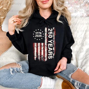 A woman wearing a black hoodie with a graphic design on it, sitting on a couch.