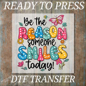 May include: A colorful DTF transfer with the text "Be the REASON someone SMILES today!" in a playful font. The design includes a pink butterfly, flowers, and polka dots, perfect for crafting projects.