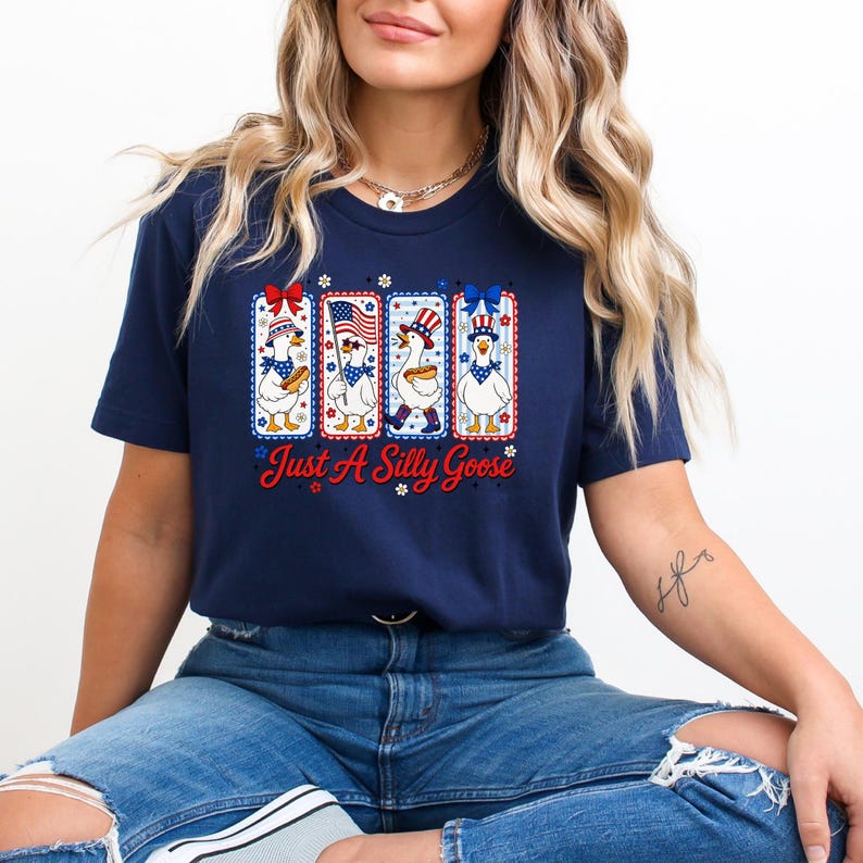 A woman wearing a navy blue t-shirt with a graphic design of four cartoon ducks and the text "Just a Silly Goose" is sitting down.