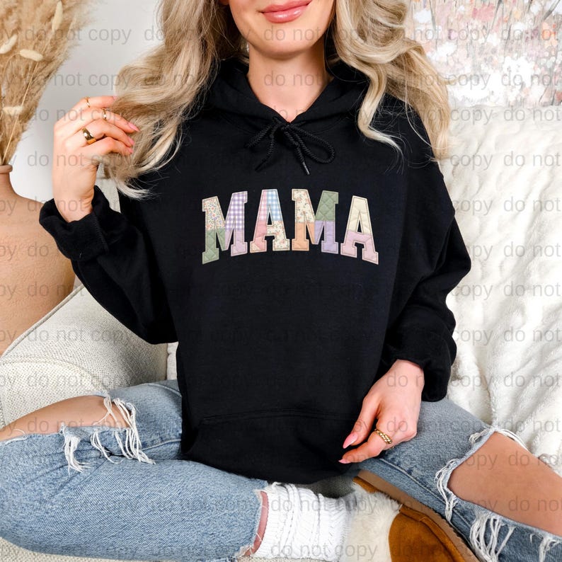 A woman wearing a black hoodie with the word "MAMA" printed on it, sitting on a couch with her legs crossed.