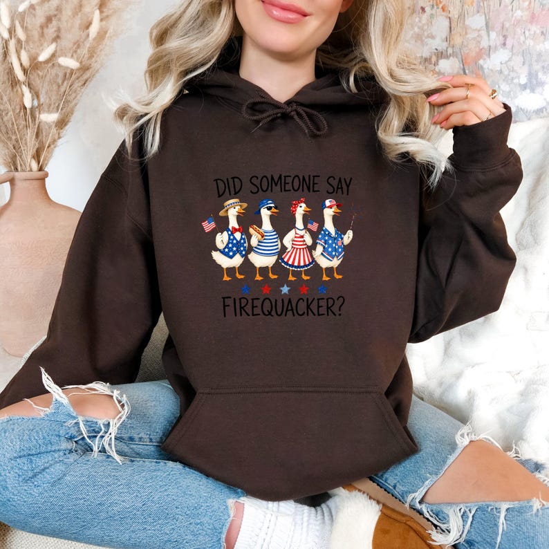 A woman wearing a brown hoodie with a graphic of four cartoon ducks and the text "Did someone say firefighter?"