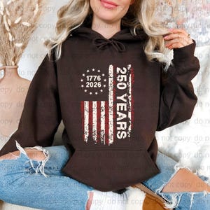 A woman wearing a brown hoodie with a graphic design on it, sitting on the floor.