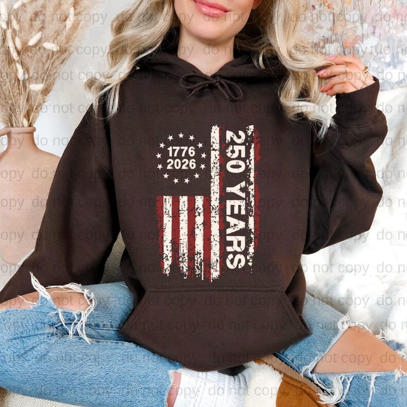 A woman wearing a brown hoodie with a graphic design on it, sitting on the floor.