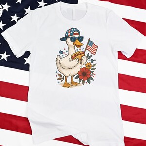 a white shirt with a duck wearing a hat and an american flag