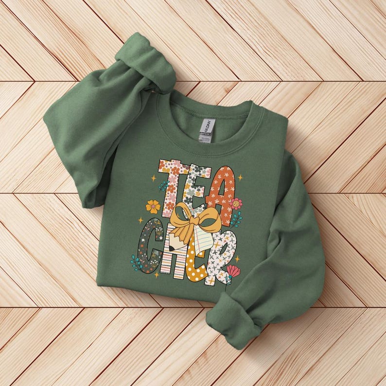 A green sweatshirt with a colorful graphic design on it, featuring the text "TEACHER" in a playful font.