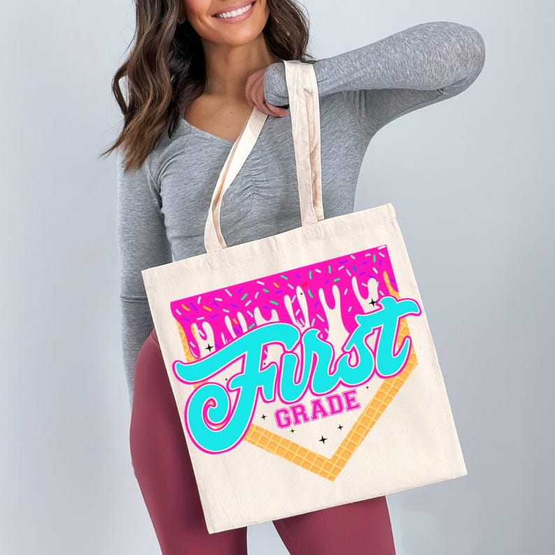 A woman is holding a large tote bag with a colorful graphic design that says "First Grade" on it.