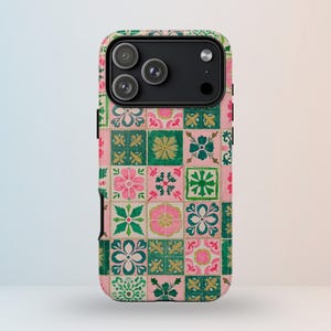 以下が含まれることがあります： カラフルなタイルのパターンが施された携帯電話ケース。ピンク、グリーン、ゴールドの花柄と幾何学模様が格子状に配置されています。ケースには黒いカメラモジュールが付いています。