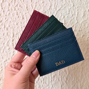 Hand holding navy, burgundy and black cardholder wallets.