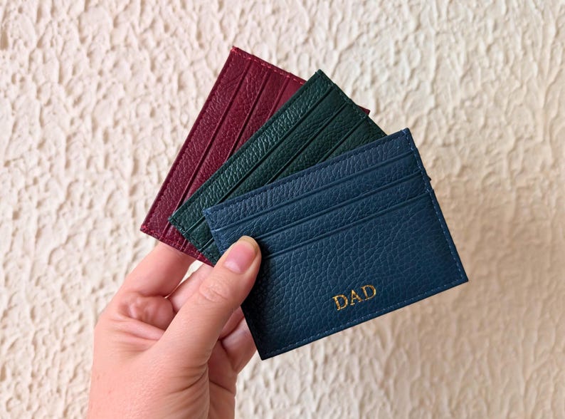 Hand holding navy, burgundy and black cardholder wallets.