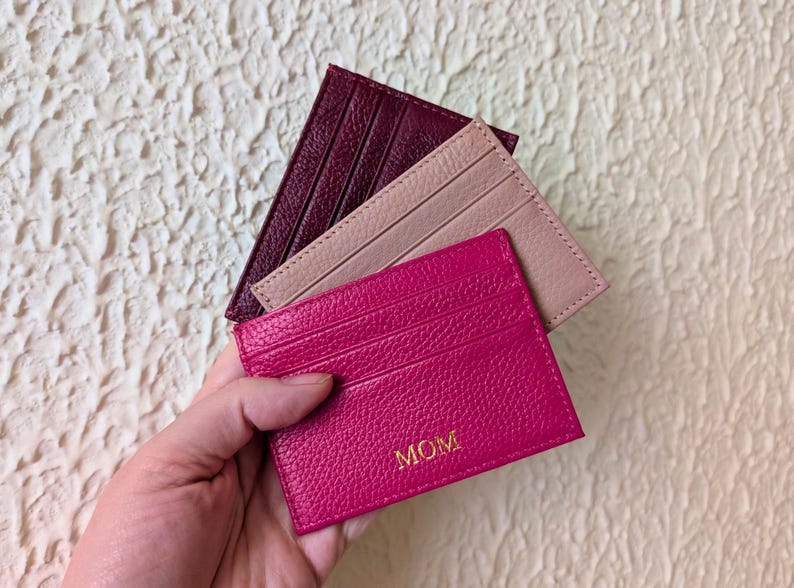 Hand holding burgundy, pink and blush cardholder wallets.