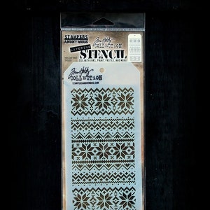 May include: A white stencil with a black snowflake and geometric pattern design. The stencil is labeled "Jim Holtz Collection Layering Stencil Holiday Knit TH5028".