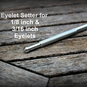 May include: A silver eyelet setter tool for 1/8 inch and 3/16 inch eyelets. The tool has a textured handle and a pointed tip. The text "Eyelet Setter for 1/8 inch & 3/16 inch Eyelets" is visible in the image.