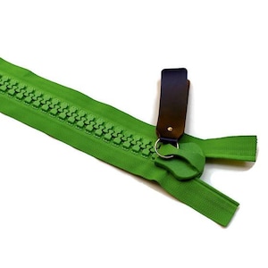 May include: A bright green zipper with a dark brown pull tab and a silver ring. The zipper teeth are a matching green color. The zipper is on a white background.