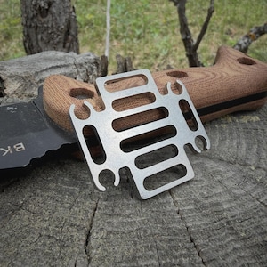 May include: A silver-colored metal multi-tool with a rectangular grid of slots and four U-shaped cutouts on the sides, resting on a black knife handle with brown textured scales that features the text BK-7 printed in white on the blade.