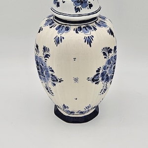 Może przedstawiać: Biały ceramiczny słoik na imbir z pokrywką, ozdobiony niebieskimi wzorami kwiatowymi. Słoik ma pękaty kształt oraz ciemnoniebieską podstawę i guz. Kwiatowy wzór powtarza się na pokrywce.