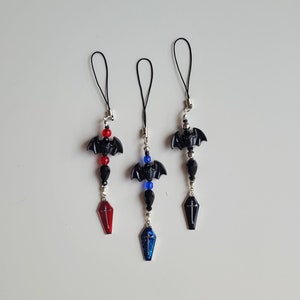 May include: Three black bat phone charms with black beads and a coffin charm. The charms are red, blue, and black.