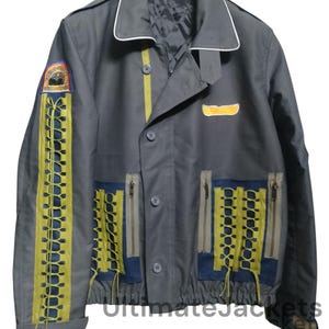 Peut inclure: Une veste grise avec des accents jaunes et bleus. La veste a une fermeture éclair et une fermeture à bouton. La veste a un patch sur la manche gauche avec un logo et le texte "WORLDWIDE". La veste a un patch sur le côté droit avec un motif d'aile jaune.