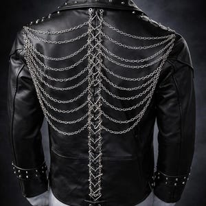 May include: A black leather jacket featuring silver-toned metal studs along the collar and cuffs. The back is decorated with a vertical central lacing system made of silver chains, flanked by multiple draped silver chain strands on each side.
