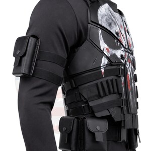 May include: Black tactical vest with a white skull design and red accents. The vest features multiple pouches and straps, along with a black arm pouch. This item is suitable for cosplay or costume use.