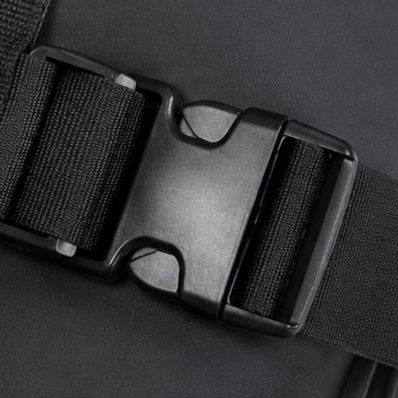 May include: Close-up of a black plastic buckle with a woven nylon strap. The buckle is rectangular with a central release mechanism. The strap is securely fastened within the buckle's frame, and the background is a dark, textured surface.