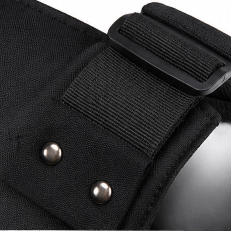 May include: Close-up of a black fabric with a black strap and buckle. Two silver metal rivets are visible on the fabric. The image highlights the texture and construction of the material.
