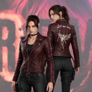 May include: A dark red leather motorcycle jacket featuring a silver zipper, a waist belt, and a lapel collar. The back of the jacket displays a white graphic of a winged figure holding a spear with the text Let me live written above it.