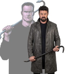 May include: A man in a long, grey leather coat holds a black crowbar. A comic book-style illustration of a man with a crowbar is in the background. The man is wearing a black shirt.
