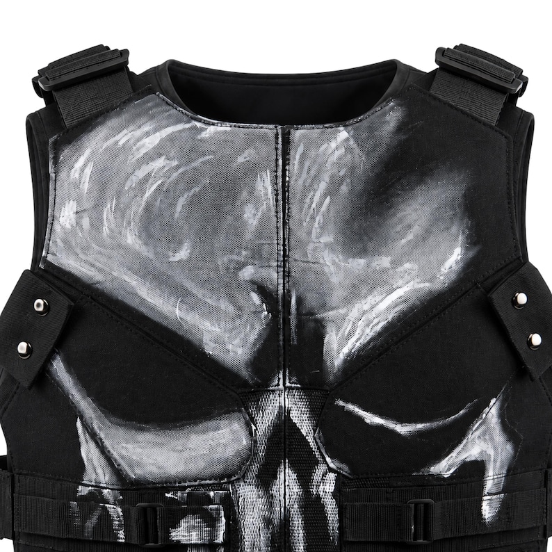 May include: Black tactical vest featuring a white skull design on the chest. The vest has adjustable straps, buckles, and a high neckline. The skull design is painted in a distressed style, adding to the vest's rugged appearance.