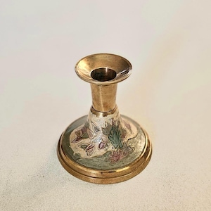 Puede incluir: Un candelero de latón con un diseño floral en tonos verdes, rosas y blancos. El candelero tiene una base ancha y una parte superior estrecha.