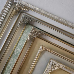 Può includere: Un assortimento di cornici ornate di varie dimensioni. Le cornici presentano intricati dettagli dorati e argentati, con accenti decorativi agli angoli. Alcune cornici hanno un bordo interno bianco o dorato e gli sfondi includono un motivo a fantasia verde chiaro.