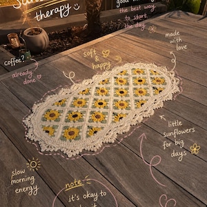 Op de afbeelding: Een ovaal gehaakt kleed met een herhalend patroon van gele en bruine zonnebloemen op een crèmekleurige achtergrond met een decoratieve schulprand. De afbeelding bevat handgeschreven tekst: Sunshine therapy, good morning, coffee, soft & happy, made with love, little sunflowers for big days, slow morning energy, en note: it's okay to take it slow.