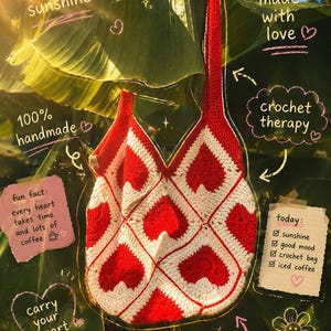 Op de afbeelding: Een rood-witte gehaakte tas met een herhalend hartjespatroon. De tas heeft een enkele schouderband en is versierd met handgeschreven tekst, waaronder "morning sunshine," "made with love," "100% handmade," "crochet therapy," "fun fact: every heart takes time and lots of coffee," "carry your heart," "soft stitches good vibes sunny days," en een checklist "today: sunshine, good mood, crochet bag, iced coffee."