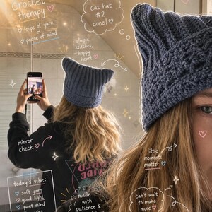 Op de afbeelding: Een donkerblauwe gehaakte muts met kattenoren en een geribbelde textuur. De muts heeft twee puntige oren aan de bovenkant en wordt op het hoofd gedragen. De afbeelding bevat handgeschreven tekst zoals Crochet therapy, Cat hat #2 done en today's vibe.