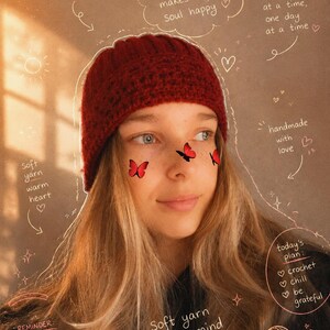 Op de afbeelding: Een donkerrode gehaakte muts met een geribbelde textuur. De afbeelding bevat handgeschreven tekst, waaronder zinnen als 'crocheting makes my soul happy', 'soft yarn warm heart', 'handmade with love' en 'today's plan: crochet, chill, be grateful'.