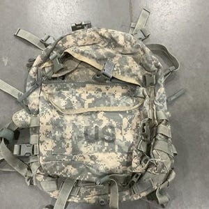 May include: A camouflage backpack with multiple straps and buckles. The backpack has a large main compartment and a smaller front pocket. The fabric is a green and brown camouflage pattern.