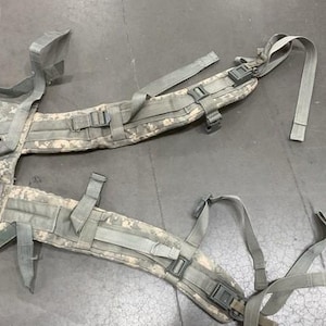 May include: A camouflage-patterned military-style backpack harness with adjustable straps and buckles.